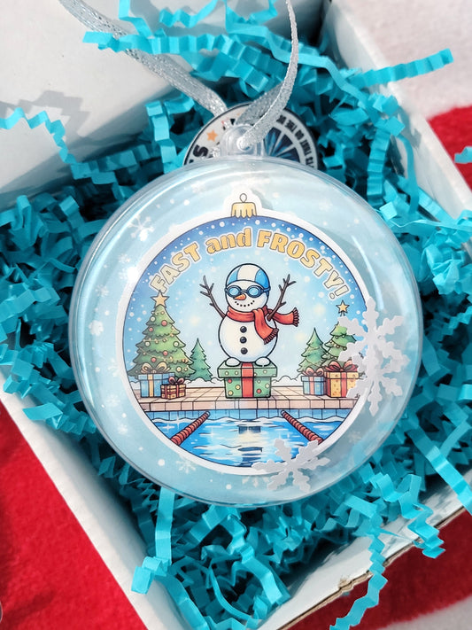 Round plastic ornament with snowman sticker inside the front and small paper confetti snowflakes and a snowy background. 