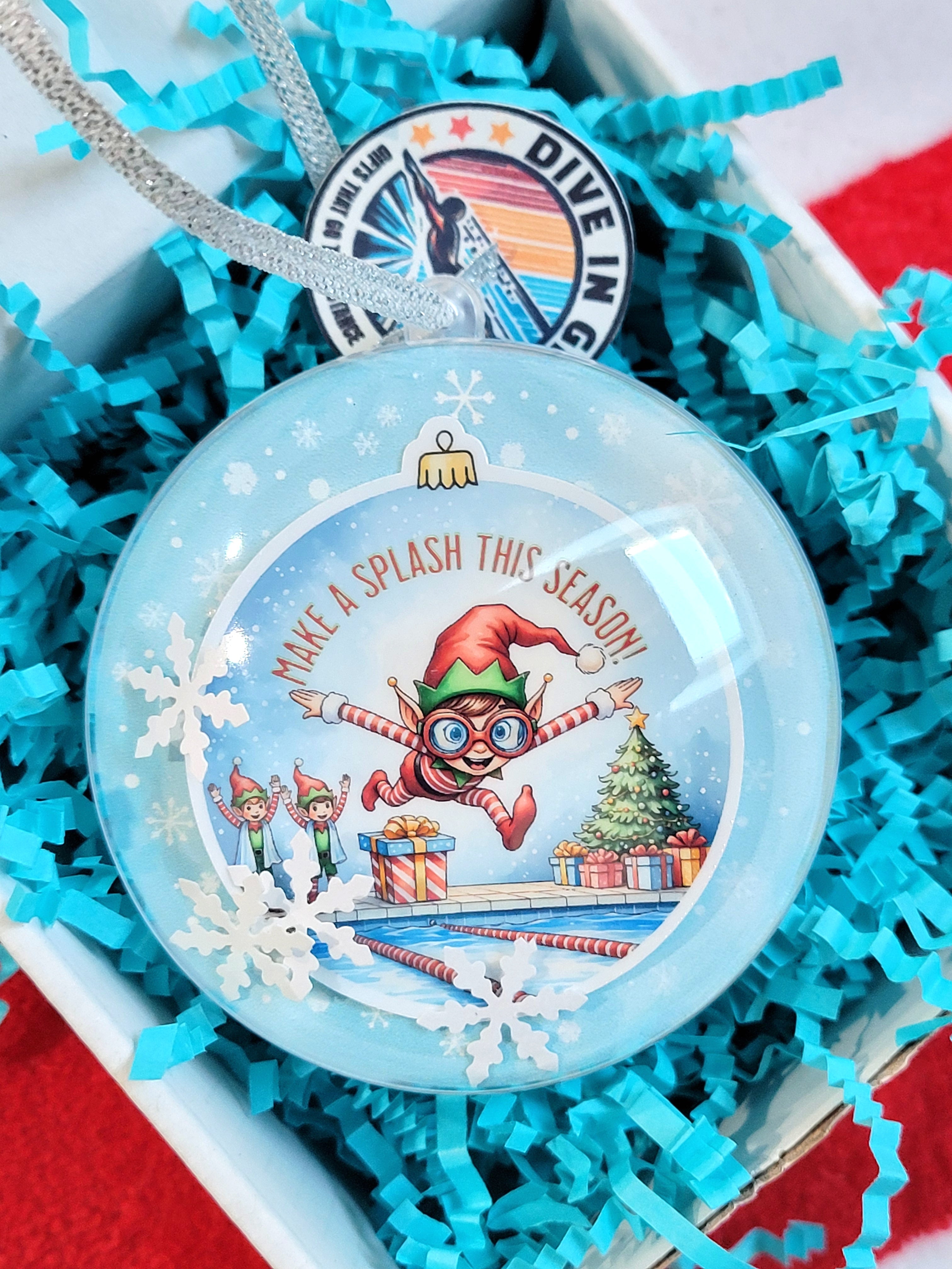 Decorative ornament with elf design and text in a gift box with blue crinkle paper.